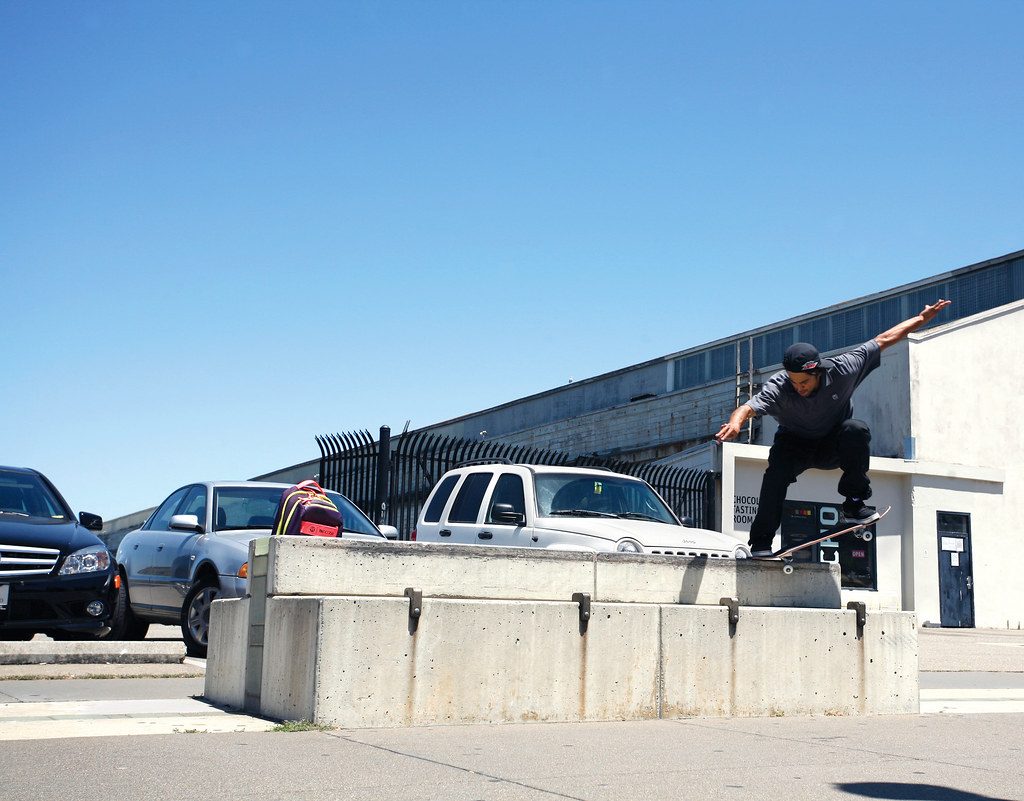 A skateboarder grinding a concrete ledge that already has metal skate stoppers installed along its edge