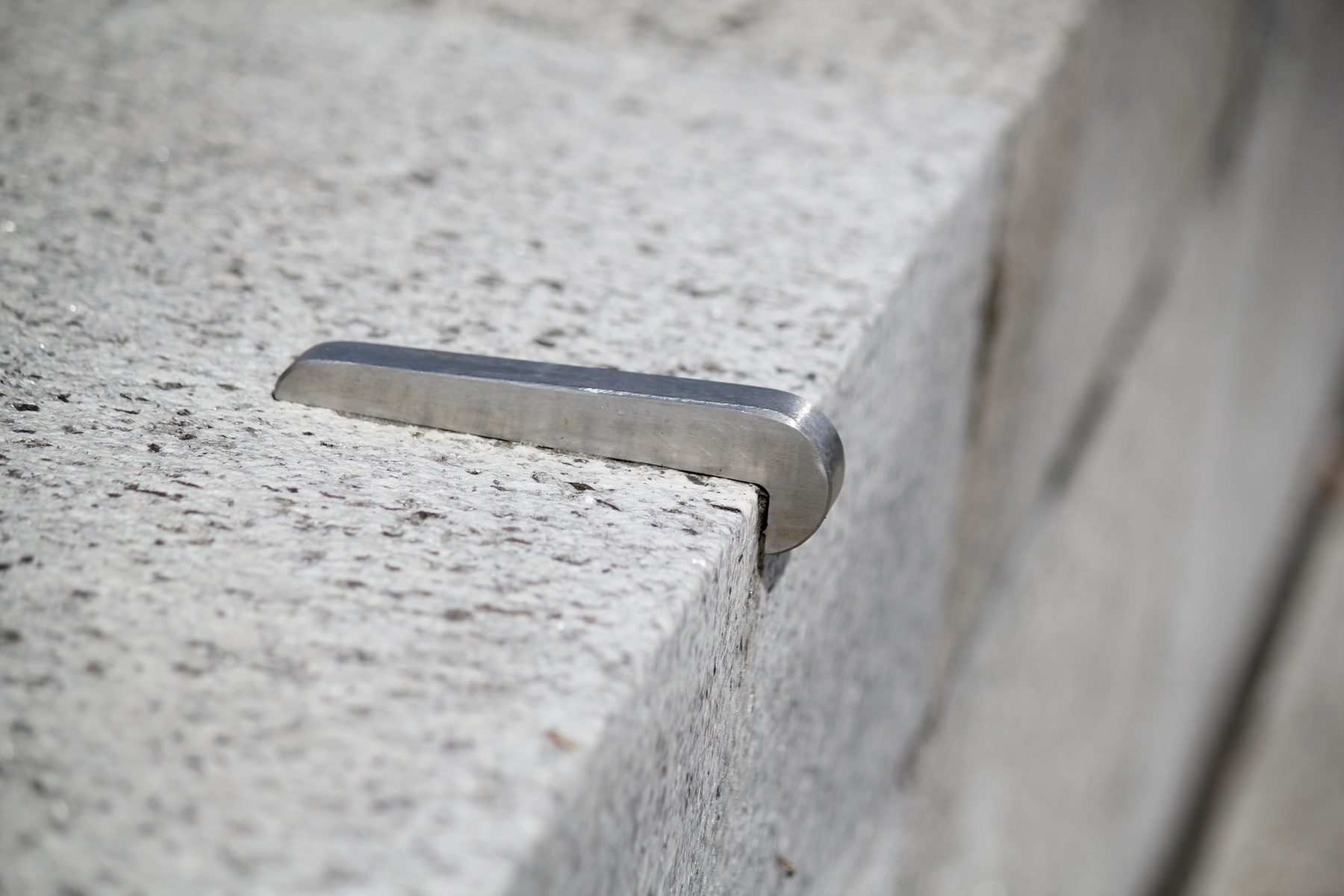 Close-up of a brushed stainless steel skate stopper bracket mounted on the edge of a granite ledge
