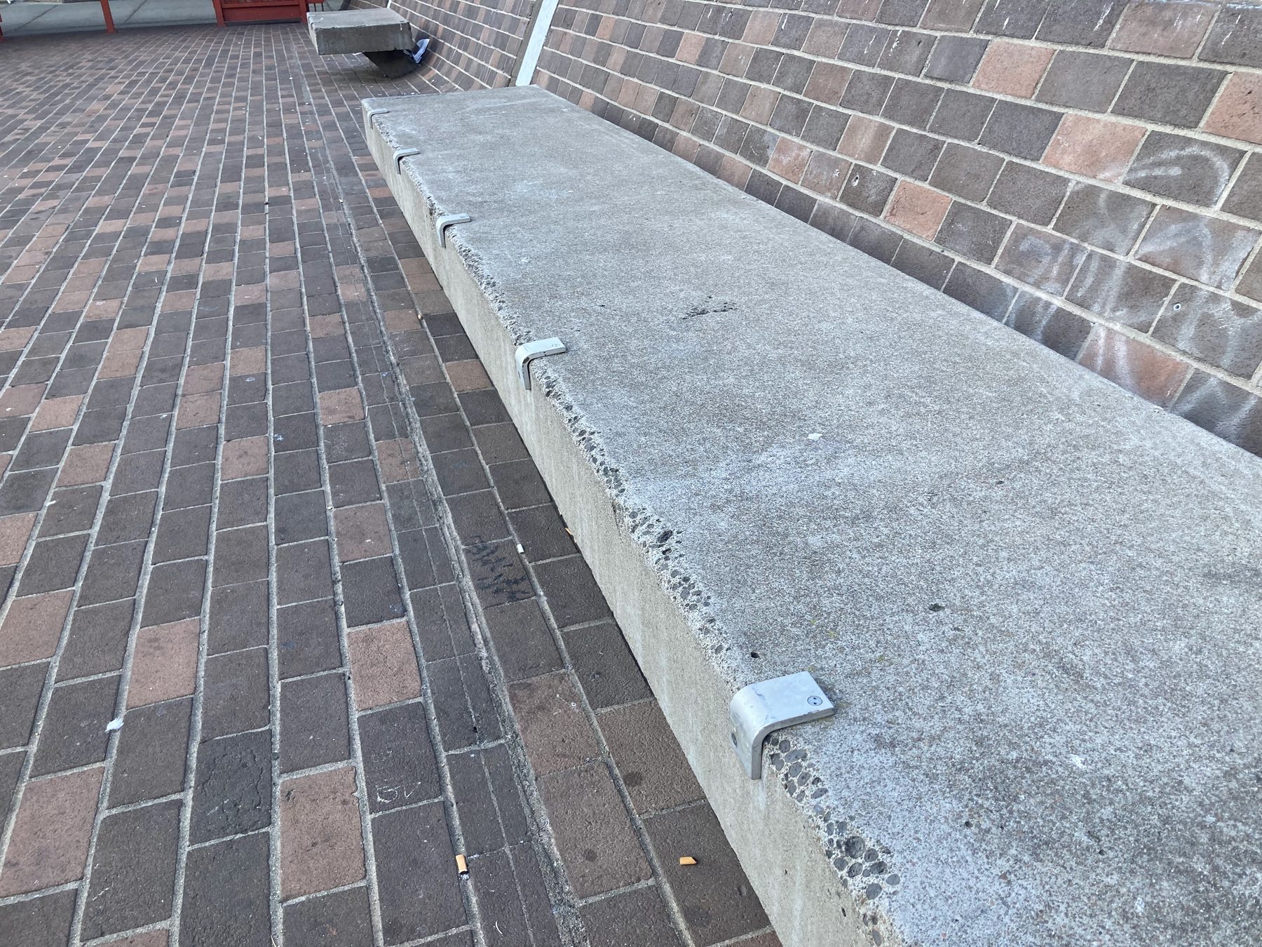 Metal skate stoppers installed along the edge of a long concrete bench in a brick plaza